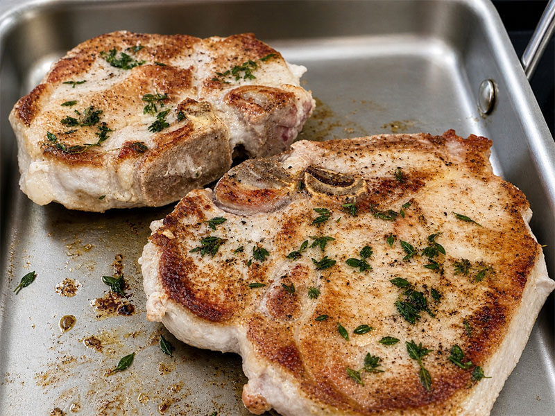 Seared herbed pork chops cooking on griddle